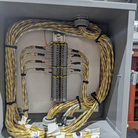 Gold-jacketed control cable bundled and tied in a loop inside an enclosure, landing on a numbered terminal strip.