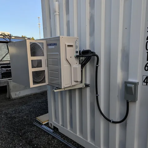 A heat pump outdoor unit mounted on a wall bracket with its disconnect switch and cable run beside it.