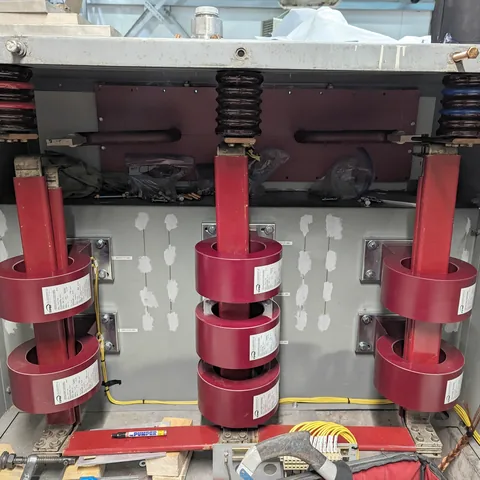 Switchgear with the covers off: three red bus risers passing through ring-type current transformers.
