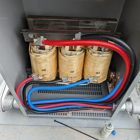 A dry-type transformer with its three windings exposed and red, blue and black cables landed on the terminals.