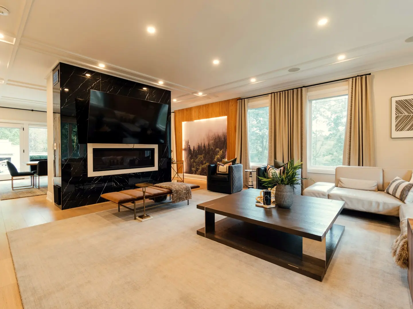A warm living room at night lit by recessed ceiling lights and a fire, with the curtains drawn.